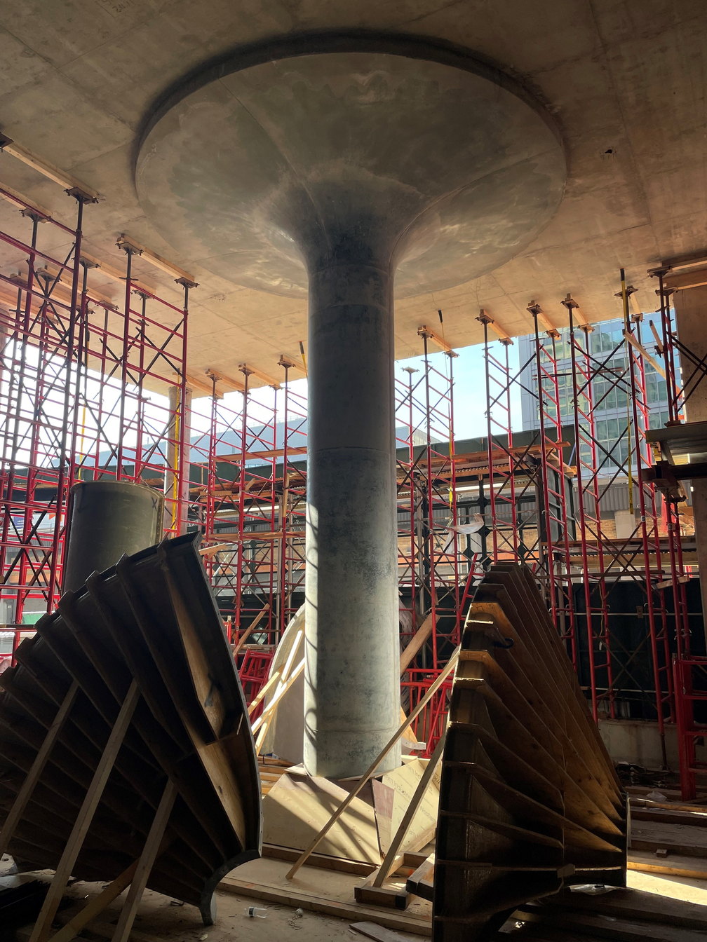 A concrete column with a flared capital on a deck under construction, shoring frames around it and curved column form sections stacked in the foreground