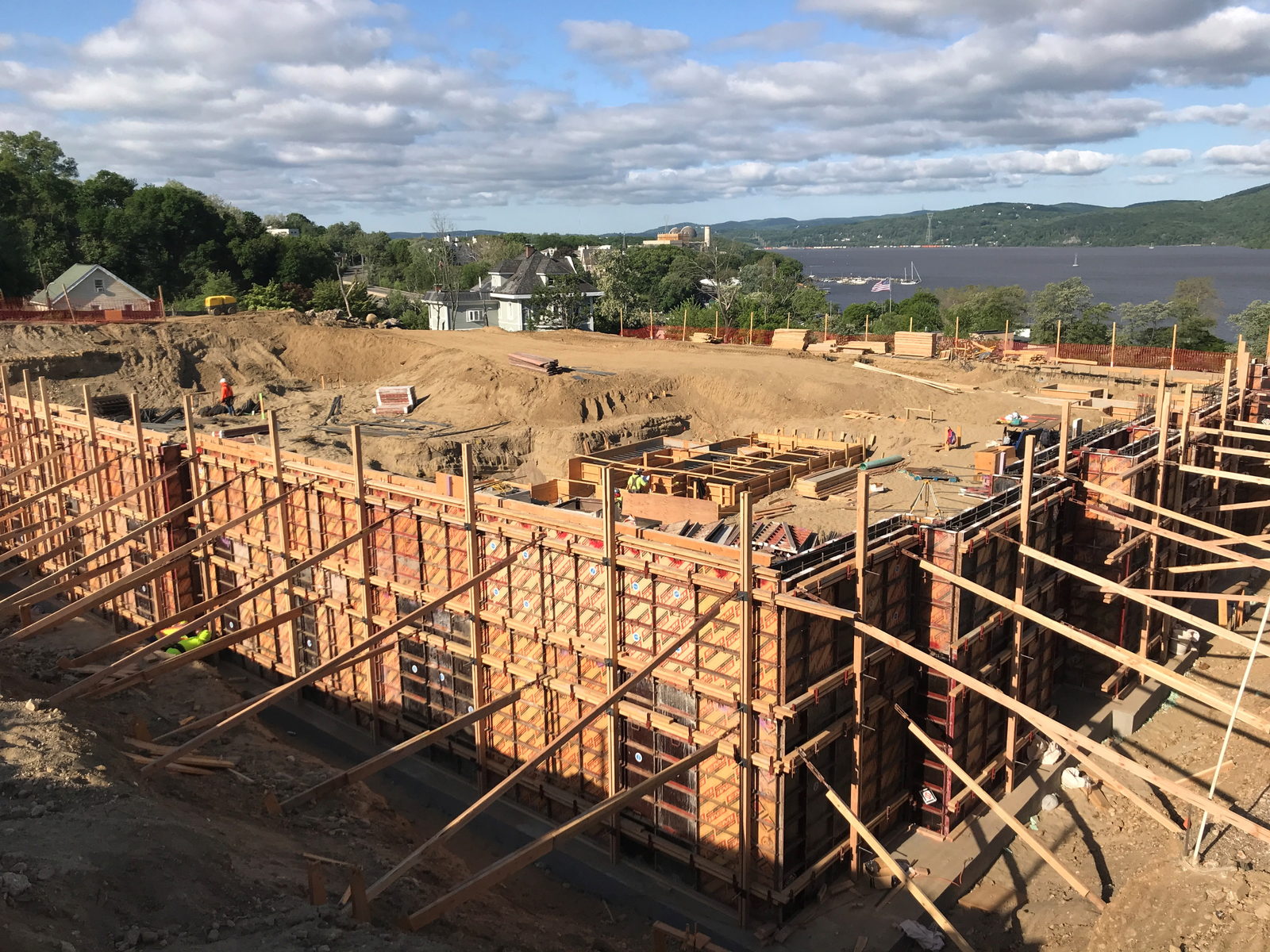 Braced wall formwork panels set out across an excavated foundation site, with a river and wooded hills in the distance