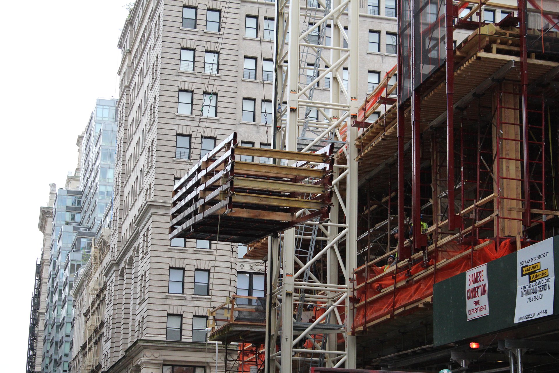 A bundle of aluminum stringers is hoisted up the building face